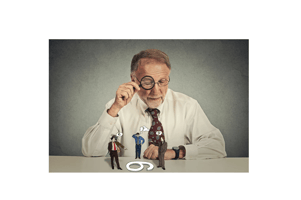 Person with glasses sitting at desk skeptically looking at group of arguing people through magnifying glass isolated grey wall background. Human expression, attitude. To each its own concept.