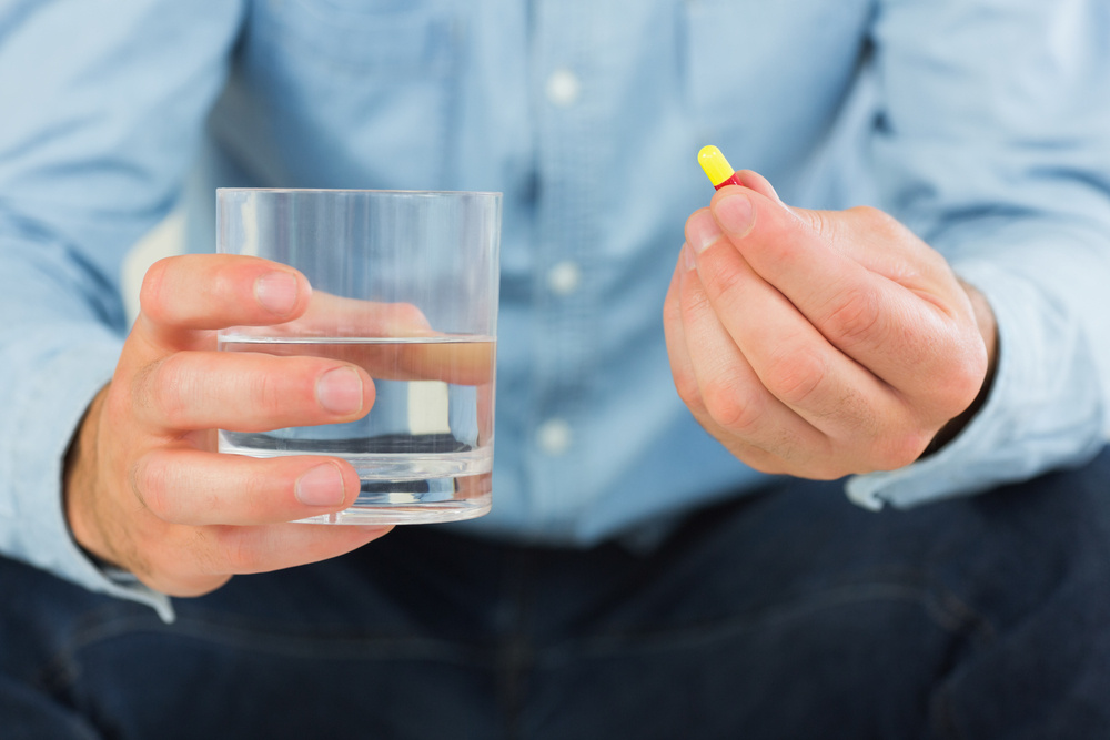 Close up of man holding a pill and glass of water in bright living room